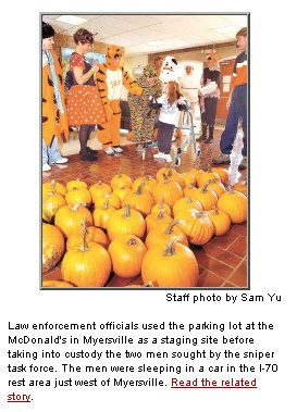 Picture of pumpkins, adults in costumes and little girl in a walker. Caption reads: Law enforcement officials used the parking lot at the McDonald's in Myersville as a staging site before taking into custody the two men sought by the sniper task force. The men were sleeping in a car in the I-70 rest area just west of Myersville. Read the related story.