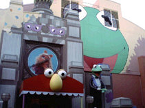 Muppet storefront with a huge Kermit on the wall, Miss Piggy above the awning and a generic Muppet loosely resembling Elmo on the awning